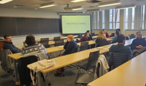 New faculty members, seated in a classroom, talking to one another.